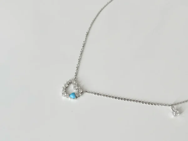 Open heart diamond necklace in sterling silver with a vibrant turquoise center stone, encircled by brilliant high-carbon diamonds, arranged in an elegant S-shape.