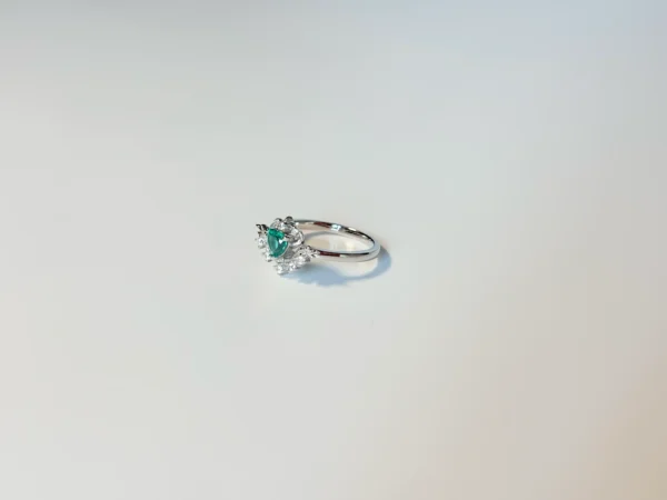 Heart-shaped emerald ring in sterling silver with rhodium plating and diamond accents on a white background